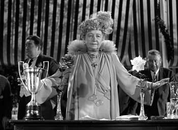 Movie still from “Mrs. Miniver” (1942), directed by William Wyler – An older woman standing in front of trophies; Medium shot, Low angle