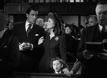 Movie still from “Mrs. Miniver” (1942), directed by William Wyler – A man and a woman are standing in front of a crowd; Medium shot, Over the shoulder angle