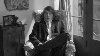 Movie still from “Much Ado About Nothing” (2012), directed by Joss Whedon – A man sitting in a chair in a room; Medium shot, Low angle