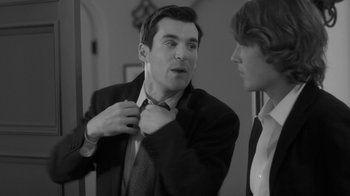 Movie still from “Much Ado About Nothing” (2012), directed by Joss Whedon – A man in a suit and tie fixing his neck tie; Medium shot, Over the shoulder angle