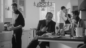 Movie still from “Much Ado About Nothing” (2012), directed by Joss Whedon – A black and white photo of a man sitting at a table; Medium shot, Over the shoulder angle