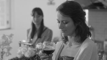 Movie still from “Much Ado About Nothing” (2012), directed by Joss Whedon – A woman holding a glass of red wine in front of another woman; Close Up shot, Over the shoulder angle