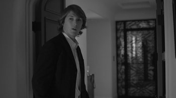 Movie still from “Much Ado About Nothing” (2012), directed by Joss Whedon – A man in a suit and tie standing in front of a door; Medium shot, Low angle