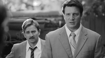 Movie still from “Much Ado About Nothing” (2012), directed by Joss Whedon – A man in a suit and tie standing next to another man in a suit and tie; Close Up shot, Over the shoulder angle