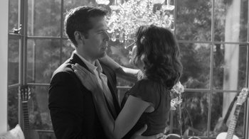 Movie still from “Much Ado About Nothing” (2012), directed by Joss Whedon – A man and a woman embracing in front of a window; Medium shot, Over the shoulder angle