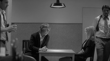 Movie still from “Much Ado About Nothing” (2012), directed by Joss Whedon – A man sitting at a table looking at a light; Medium shot, Over the shoulder angle