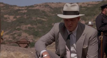 Movie still from “Mulholland Falls” (1996), directed by Lee Tamahori – A man in a suit and a hat sitting on the ground; Medium shot, Low angle