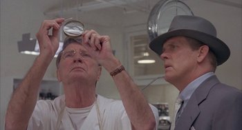 Movie still from “Mulholland Falls” (1996), directed by Lee Tamahori – A man looking through a magnifying glass at another man wearing a hat; Close Up shot, Low angle