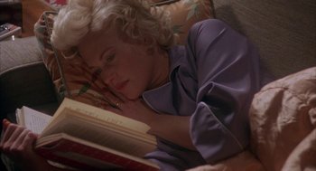 Movie still from “Mulholland Falls” (1996), directed by Lee Tamahori – A woman laying on a bed reading a book; Medium shot, High angle