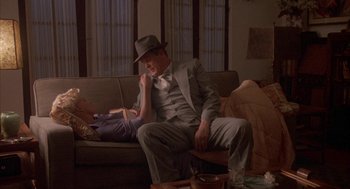 Movie still from “Mulholland Falls” (1996), directed by Lee Tamahori – A man in a suit and hat sitting on a couch; Medium shot, High angle