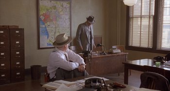 Movie still from “Mulholland Falls” (1996), directed by Lee Tamahori – Two men in suits and hats are sitting at a desk; Wide shot, High angle