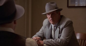 Movie still from “Mulholland Falls” (1996), directed by Lee Tamahori – A man in a suit and a hat sitting in front of another man in a suit; Close Up shot, Over the shoulder angle
