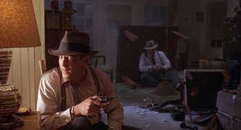 Movie still from “Mulholland Falls” (1996), directed by Lee Tamahori – A man sitting on the ground holding a gun; Medium shot, Low angle