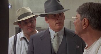 Movie still from “Mulholland Falls” (1996), directed by Lee Tamahori – A man in a suit and a hat is talking to two other men; Close Up shot, Over the shoulder angle