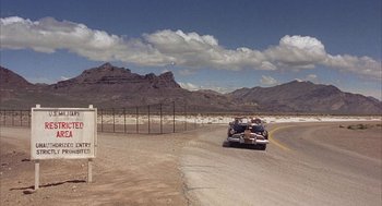 Movie still from “Mulholland Falls” (1996), directed by Lee Tamahori – A car driving down a road in the middle of the desert; Extreme Wide shot, Over the shoulder angle