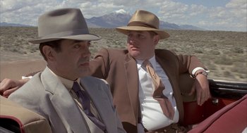 Movie still from “Mulholland Falls” (1996), directed by Lee Tamahori – A couple of men sitting next to each other on top of a field; Medium shot, Low angle