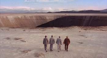 Movie still from “Mulholland Falls” (1996), directed by Lee Tamahori – A group of men in suits and hats walking across a barren area; Extreme Wide shot, High angle