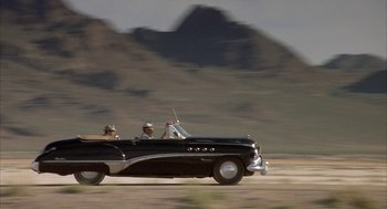 Movie still from “Mulholland Falls” (1996), directed by Lee Tamahori – Two men riding in the back of an old car; Extreme Wide shot, Low angle