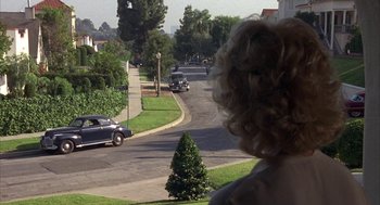 Movie still from “Mulholland Falls” (1996), directed by Lee Tamahori – A woman looking out over a street with cars driving down it; Extreme Wide shot, Over the shoulder angle