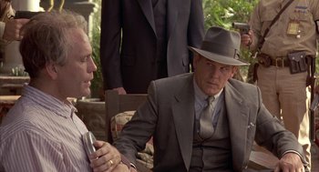 Movie still from “Mulholland Falls” (1996), directed by Lee Tamahori – A man in a suit and a hat talking to another man in a suit and a hat; Medium shot, Over the shoulder angle