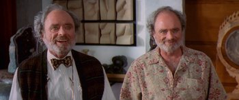 Movie still from “Multiplicity” (1996), directed by Harold Ramis – Two men standing next to each other in front of a painting; Medium shot, High angle