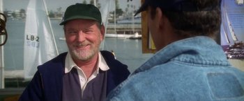 Movie still from “Multiplicity” (1996), directed by Harold Ramis – A man wearing a green hat is smiling at another man in front of a body of water; Close Up shot, Over the shoulder angle