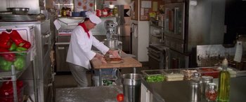 Movie still from “Multiplicity” (1996), directed by Harold Ramis – A man in a kitchen preparing food on a cutting board; Wide shot, High angle