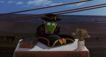 Movie still from “Muppet Treasure Island” (1996), directed by David Lane – A person sitting on top of a table wearing a pirate hat; Medium shot, High angle