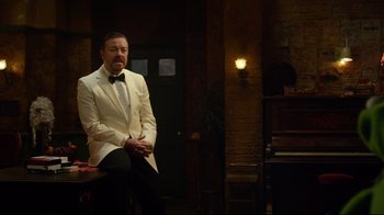 Movie still from “Muppets Most Wanted” (2014), directed by James Bobin – A man in a white suit sitting on a stool; Medium shot, High angle