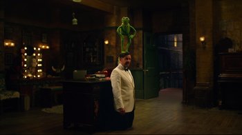 Movie still from “Muppets Most Wanted” (2014), directed by James Bobin – A man standing next to a desk with a green puppet on top of his head; Wide shot, Low angle