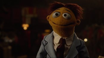 Movie still from “Muppets Most Wanted” (2014), directed by James Bobin – The face of a stuffed animal wearing a suit and tie; Close Up shot, Over the shoulder angle