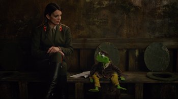 Movie still from “Muppets Most Wanted” (2014), directed by James Bobin – A woman sitting next to a stuffed animal on top of a bench; Medium shot, Over the shoulder angle