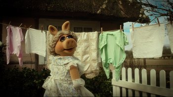 Movie still from “Muppets Most Wanted” (2014), directed by James Bobin – A person dressed as miss piggy standing next to clothes on a clothesline; Medium shot, High angle