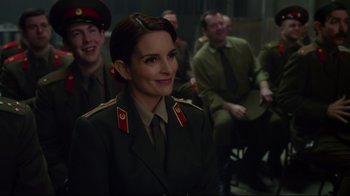 Movie still from “Muppets Most Wanted” (2014), directed by James Bobin – A group of people sitting in a room with a woman in a uniform; Medium shot, Over the shoulder angle