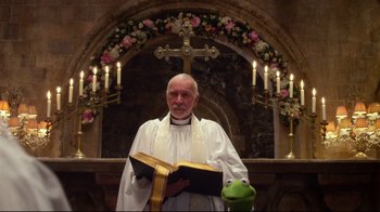 Movie still from “Muppets Most Wanted” (2014), directed by James Bobin – A priest is holding a bible in front of a cross; Medium shot, Low angle