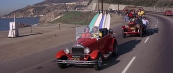 Movie still from “Muscle Beach Party” (1964), directed by William Asher – Two people in a red car with surfboards on the back of the car; Wide shot, High angle