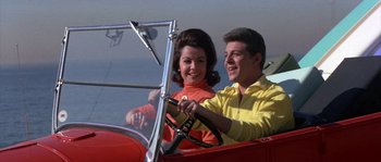 Movie still from “Muscle Beach Party” (1964), directed by William Asher – A man and a woman driving a red car; Medium shot, Low angle