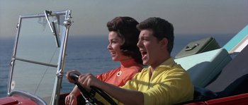 Movie still from “Muscle Beach Party” (1964), directed by William Asher – A man and a woman driving a car on the beach; Medium shot, Low angle