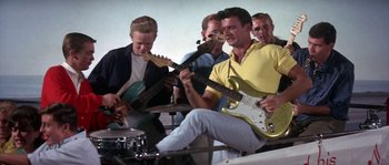 Movie still from “Muscle Beach Party” (1964), directed by William Asher – A group of men playing instruments in a band; Medium shot, Low angle