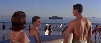 Movie still from “Muscle Beach Party” (1964), directed by William Asher – A group of people on the beach with surfboards; Medium shot, Low angle