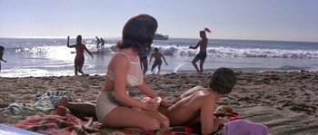 Movie still from “Muscle Beach Party” (1964), directed by William Asher – A woman in a white bathing suit on the beach with a man; Wide shot, High angle