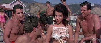 Movie still from “Muscle Beach Party” (1964), directed by William Asher – A man and a woman sitting next to each other on the beach; Medium shot, High angle