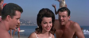 Movie still from “Muscle Beach Party” (1964), directed by William Asher – A man and a woman standing next to each other on the beach; Medium shot, Low angle