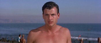 Movie still from “Muscle Beach Party” (1964), directed by William Asher – A man with no shirt is standing on the beach; Close Up shot, Low angle