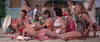 Movie still from “Muscle Beach Party” (1964), directed by William Asher – A group of people sitting on the beach in the sand; Wide shot, High angle