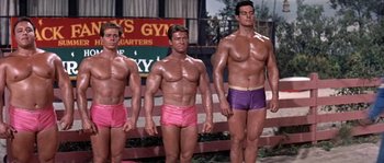 Movie still from “Muscle Beach Party” (1964), directed by William Asher – A group of men standing next to each other in their underwear; Medium shot, Low angle