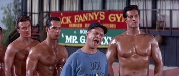 Movie still from “Muscle Beach Party” (1964), directed by William Asher – A group of shirtless men standing next to each other in a gym; Medium shot, Low angle