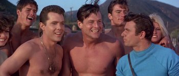 Movie still from “Muscle Beach Party” (1964), directed by William Asher – A group of shirtless men standing next to each other on a beach; Medium shot, Low angle