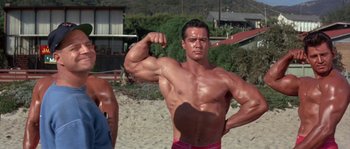 Movie still from “Muscle Beach Party” (1964), directed by William Asher – A man is showing off his muscles on the beach; Medium shot, Low angle