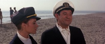 Movie still from “Muscle Beach Party” (1964), directed by William Asher – A man and a woman wearing hats standing next to each other on the beach; Medium shot, Low angle